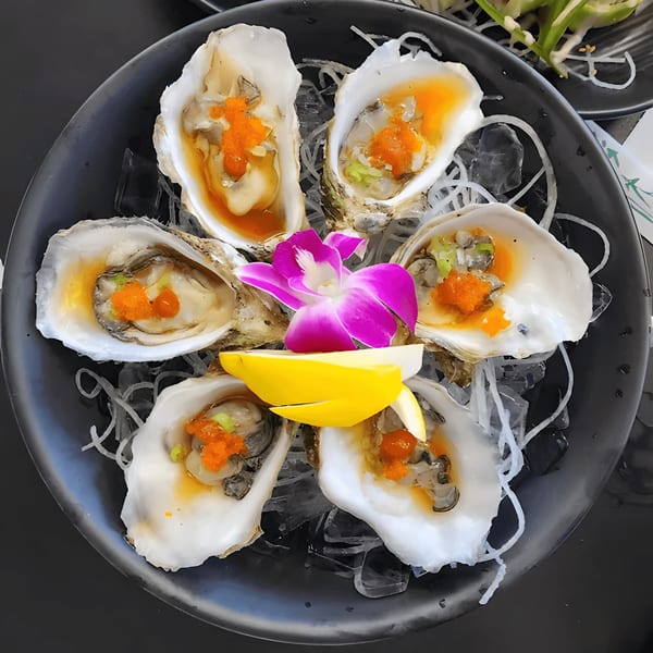 Six fresh oysters on the half shell with roe, lemon, and a purple orchid on ice.