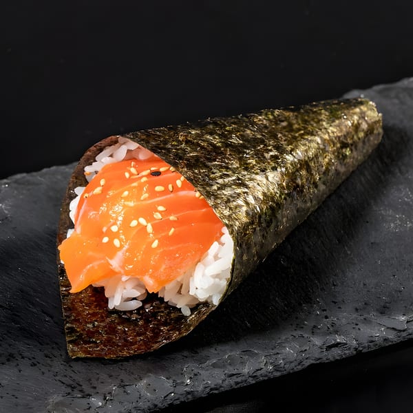 A salmon temaki hand roll with rice and sesame seeds, presented on a dark slate surface.