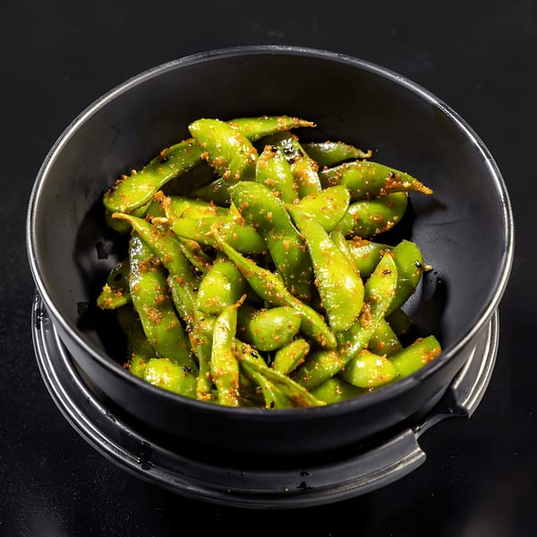 A black bowl filled with bright green edamame pods, seasoned with spices, on a dark surface.