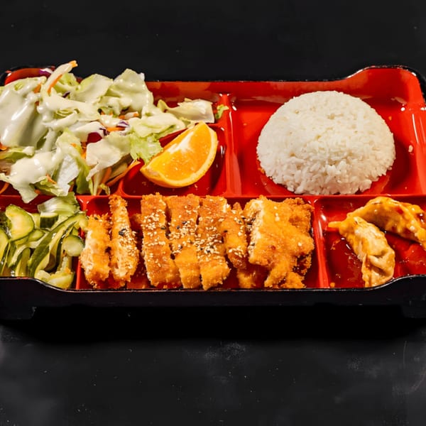 A red bento box with chicken teriyaki, white rice, salad, cucumber salad, gyoza, and an orange slice.