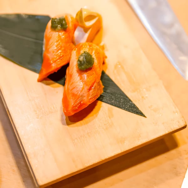 Three pieces of salmon nigiri sushi with green topping on a wooden board with a leaf.