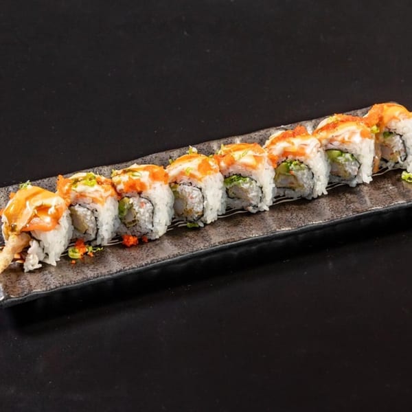 A row of sushi rolls with white rice, orange sauce, and green garnishes on a dark plate.