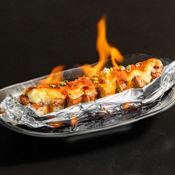 Flaming Express Sushi & Teriyaki sushi roll with melted cheese, sauce, and roe on foil.