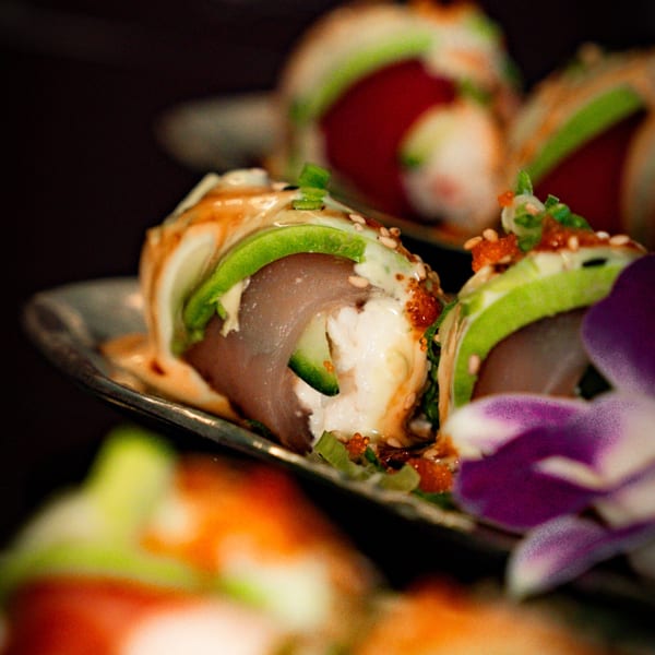 Close-up of sushi rolls with tuna, avocado, and sauce, garnished with a purple orchid.