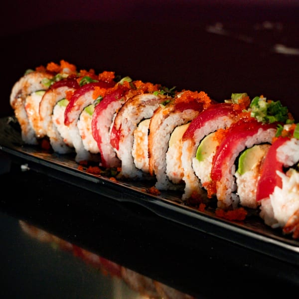 A long platter of sushi rolls, topped with red tuna, avocado, roe, and green onions.