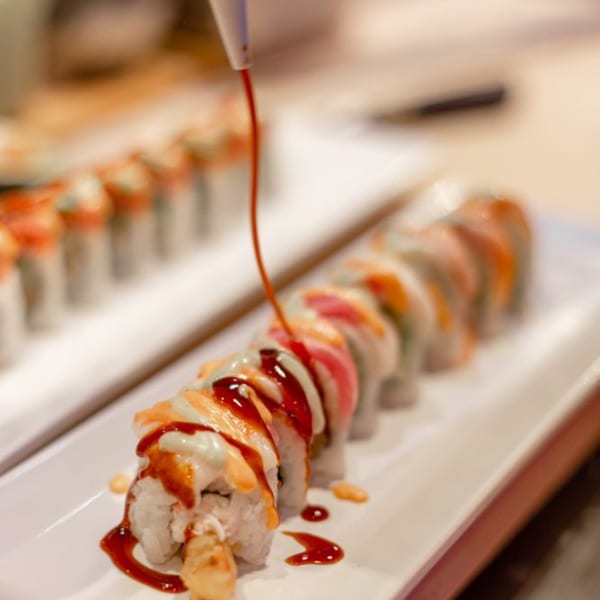 Soy sauce being drizzled over a long plate of sushi rolls with various toppings at Express Sushi.