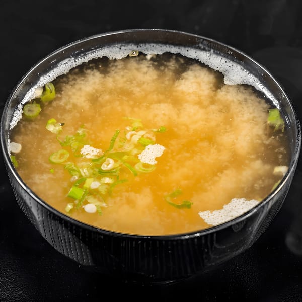 A close-up of a bowl of miso soup with green onions and tofu, from Express Sushi & Teriyaki.