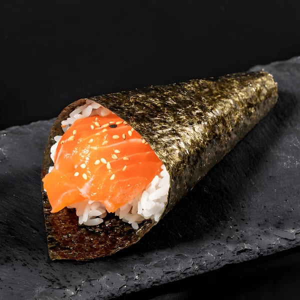 A salmon temaki hand roll with rice and sesame seeds, presented on a dark slate surface.
