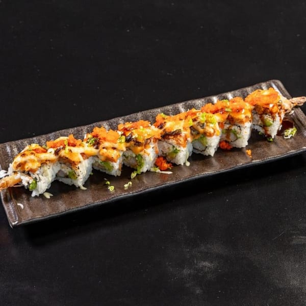 A long, dark rectangular plate holds eight pieces of sushi with shrimp tails, sauce, and roe.